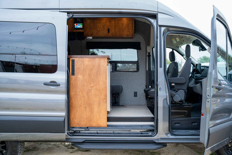 RV rental: See inside a modern camper van conversion with an open side door, showcasing its kitchen, control panel, & comfy seating.