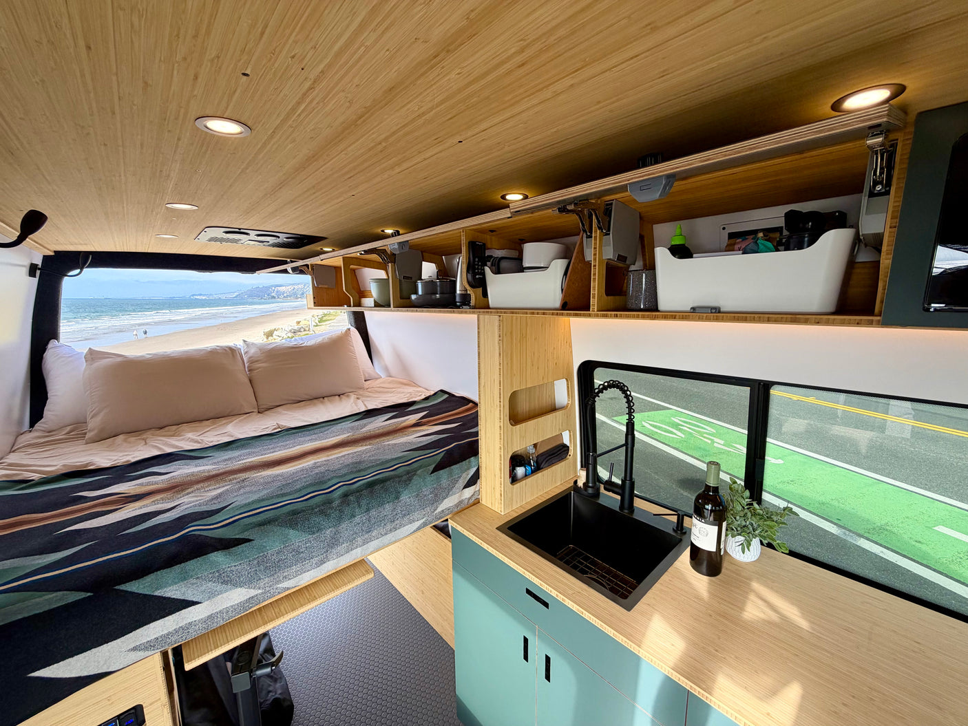 Inside a stylish **rv rental**: a comfortable bed overlooking the beach and a compact kitchen with a view of the road.