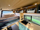 Inside a stylish **rv rental**: a comfortable bed overlooking the beach and a compact kitchen with a view of the road.