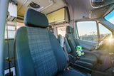 RV rental: Bright camper van interior with front seats, plushie on driver's, custom controls, and living area. Sunlit dashboard.