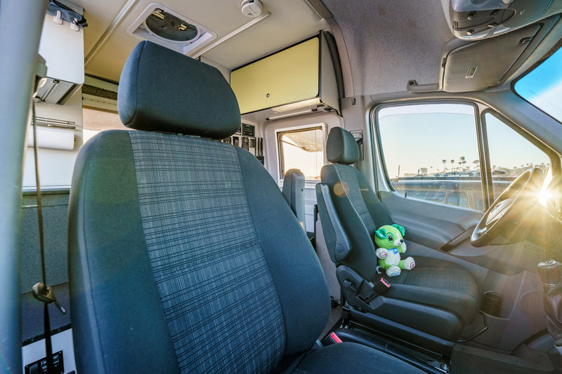 RV rental: Bright camper van interior with front seats, plushie on driver's, custom controls, and living area. Sunlit dashboard. — photo 11