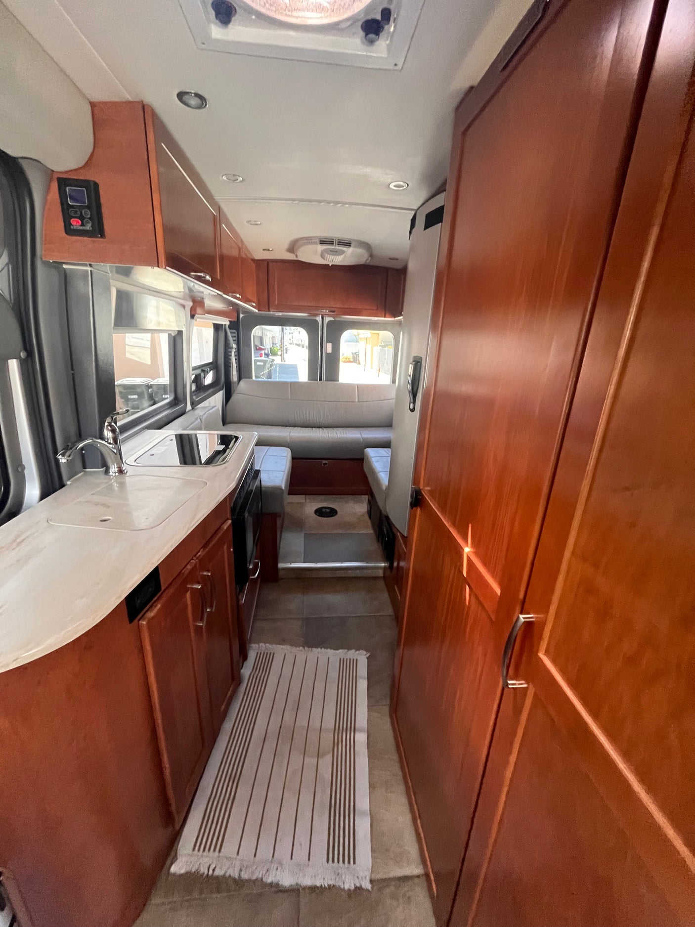 Spacious rv rental interior featuring a compact kitchen with sink, stovetop, ample wood cabinetry, and comfortable rear seating.