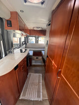 Spacious rv rental interior featuring a compact kitchen with sink, stovetop, ample wood cabinetry, and comfortable rear seating.