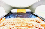 Comfortable RV rental bed setup with a knitted blanket, yellow pillow, and bright window for travel.