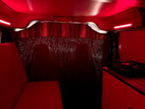 Inside a unique RV rental: red lights illuminate cozy seating, a DJ setup, and subtle shadows on patterned walls.