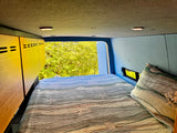 Inside this cozy RV rental, a comfy quilted bed faces lush green nature views through the open back.