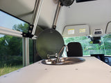 This RV rental interior showcases a compact kitchen area with a stainless steel sink, faucet, and a light countertop. A mesh window overlooks green trees outside.