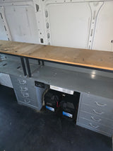 Interior of an rv rental showing a custom workbench with labeled drawers and a power system with batteries and an inverter.