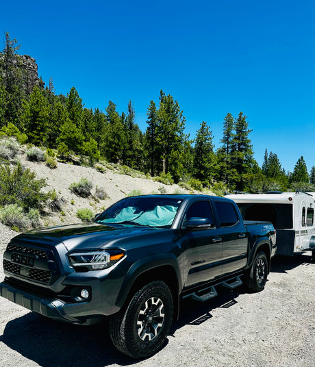 Dark grey Toyota Tacoma pickup truck towing a white small camper trailer, ideal for an RV rental outdoor adventure.