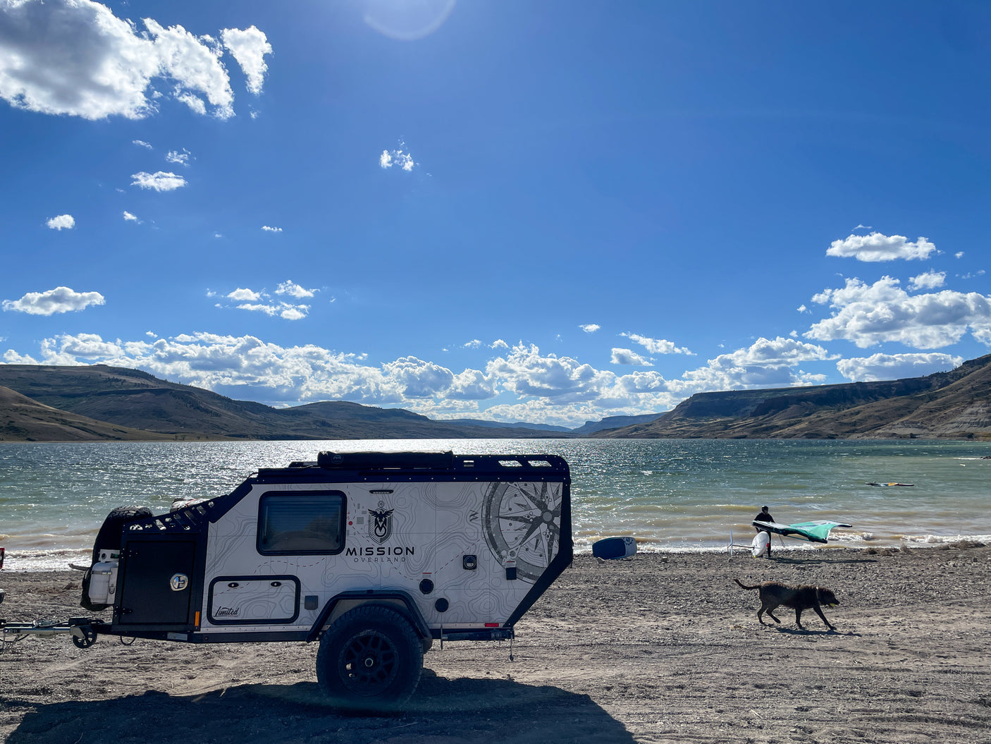 Overlanding RV rental by a lake, offering adventure with watersports, scenic mountains & a playful dog.