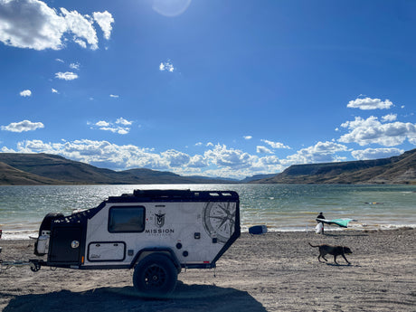 Overlanding RV rental by a lake, offering adventure with watersports, scenic mountains & a playful dog.