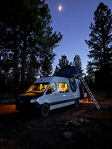 Night camping with an RV rental: a lit camper van, rooftop tent, and people under a moonlit sky.