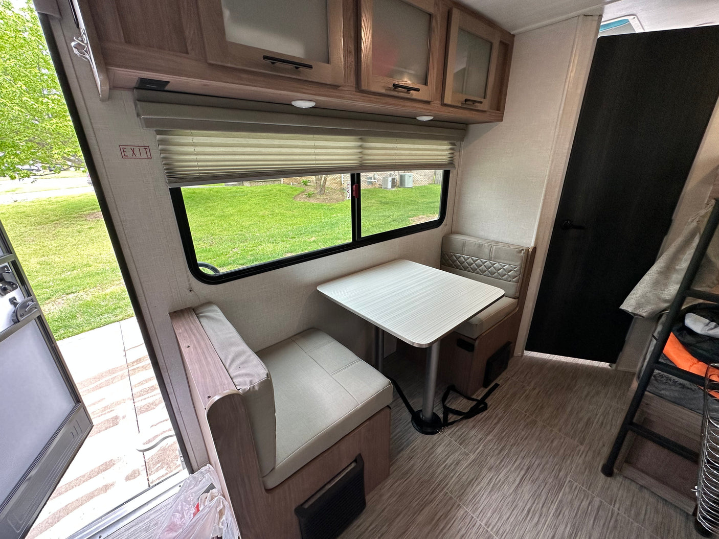 Interior of an RV rental: Dinette with table, padded benches, window view, and upper storage cabinets.