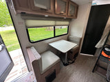 Interior of an RV rental: Dinette with table, padded benches, window view, and upper storage cabinets.