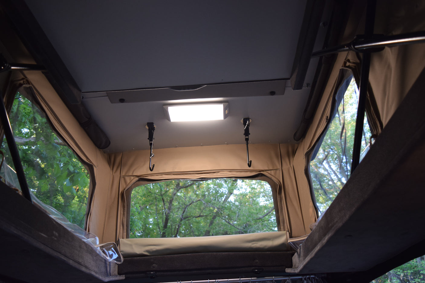 Inside an RV rental pop-up tent, showing interior light, hooks, and windows with green trees outside.
