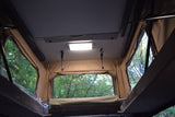 Inside an RV rental pop-up tent, showing interior light, hooks, and windows with green trees outside.