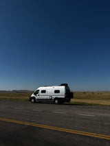 White camper van (RV rental) parked by a road in a vast, sunny landscape with hills. Perfect for your next adventure!