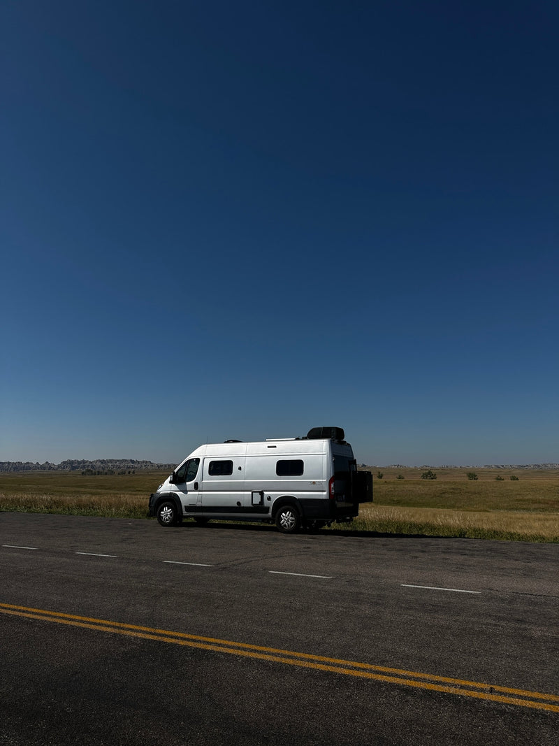  sunny landscape with hills. Perfect for your next adventure!|Cozy RV rental bed with open doors revealing epic badlands. Interior shows AC unit — photo 3