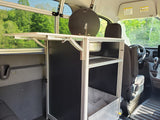 Inside an RV rental, a custom van conversion features a compact mobile kitchen unit with a sink, shelving, and a fold-out table.