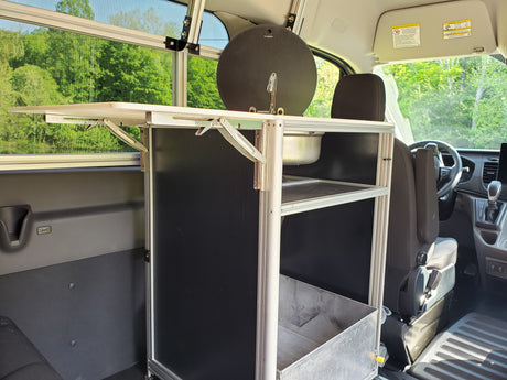 Inside an RV rental, a custom van conversion features a compact mobile kitchen unit with a sink, shelving, and a fold-out table.