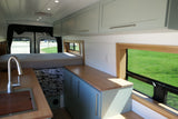 Modern RV rental interior showcasing a bed, sink, light blue cabinets, and wooden accents, perfect for van life.