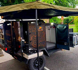 Get ready for adventure! This black off-road trailer RV rental has an open kitchen, sleeping area, and shade awning.