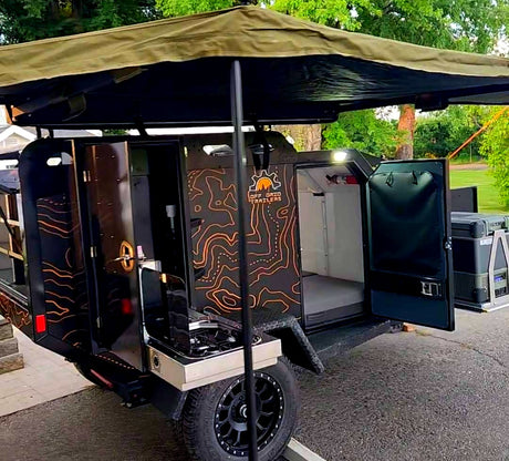 Get ready for adventure! This black off-road trailer RV rental has an open kitchen, sleeping area, and shade awning.