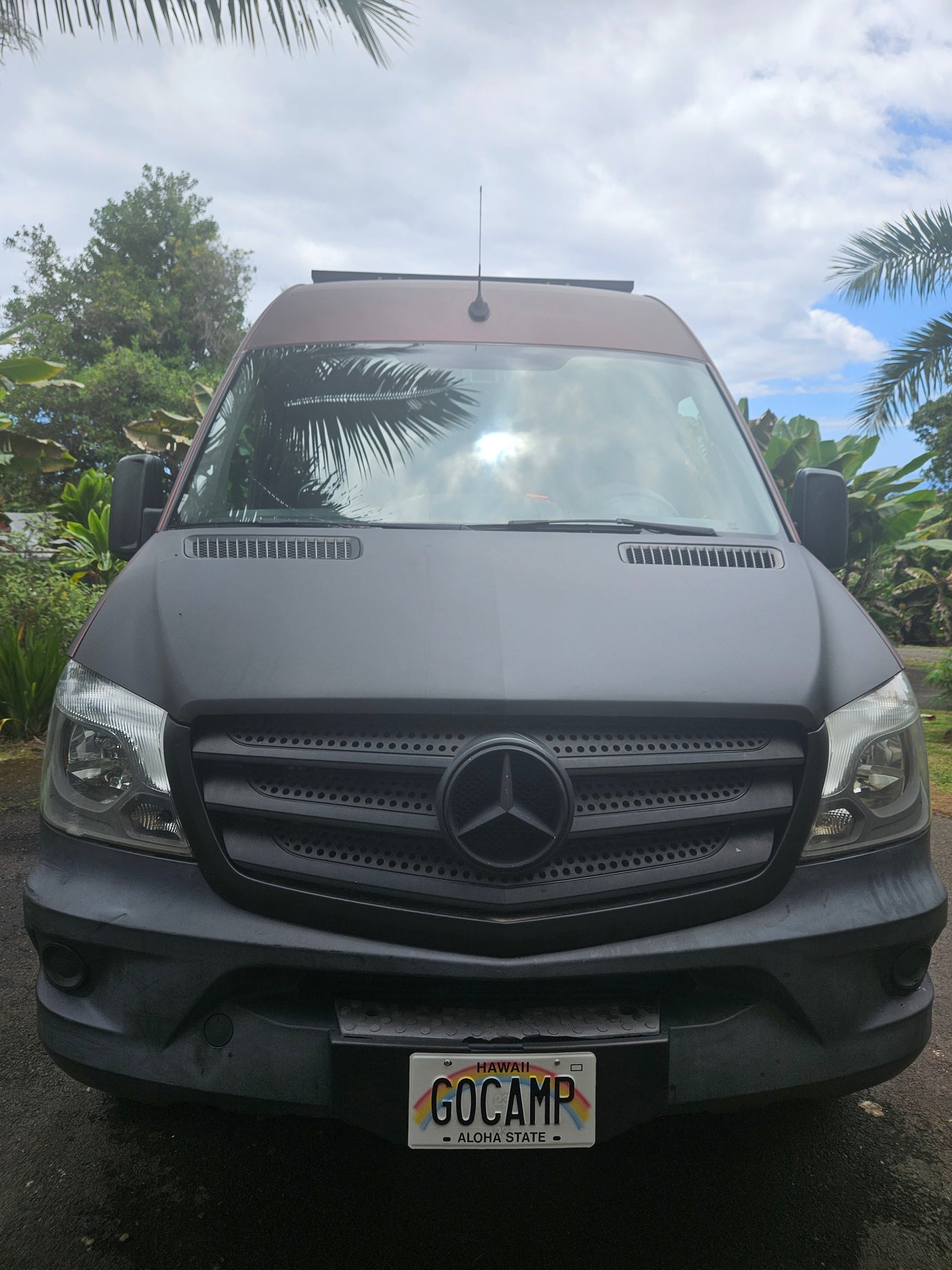 Front view of a dark Mercedes Sprinter RV rental with a "GOCAMP" Hawaii license plate, ideal for island adventures.