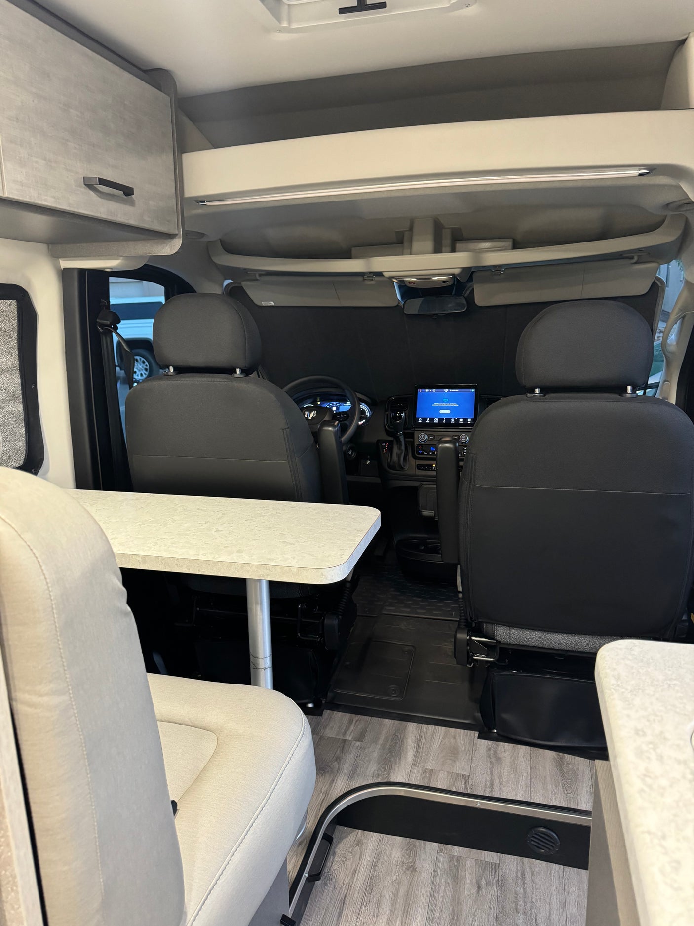 Explore this modern RV rental interior: comfortable seating, a versatile table, and driver's cockpit view.