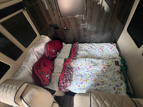 An RV rental's cozy sleeping area with patterned blankets, Arkansas Razorback pillows, and quilted seats for comfort.