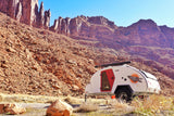 A teardrop **RV rental** trailer in a vibrant red rock desert landscape, ready for outdoor **camping** amidst majestic mountains.