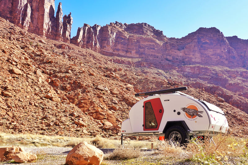 A teardrop **RV rental** trailer in a vibrant red rock desert landscape, ready for outdoor **camping** amidst majestic mountains. — photo 7