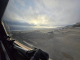 Peeking out our RV rental window to a vast sandy beach, ocean, and cloudy sky. Serene coastal landscape.