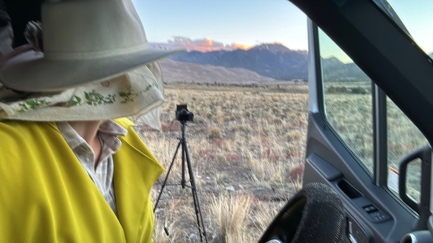 RV rental: Outdoors adventurer in hat enjoys scenic mountain views from inside, with camera on tripod for landscape photography.