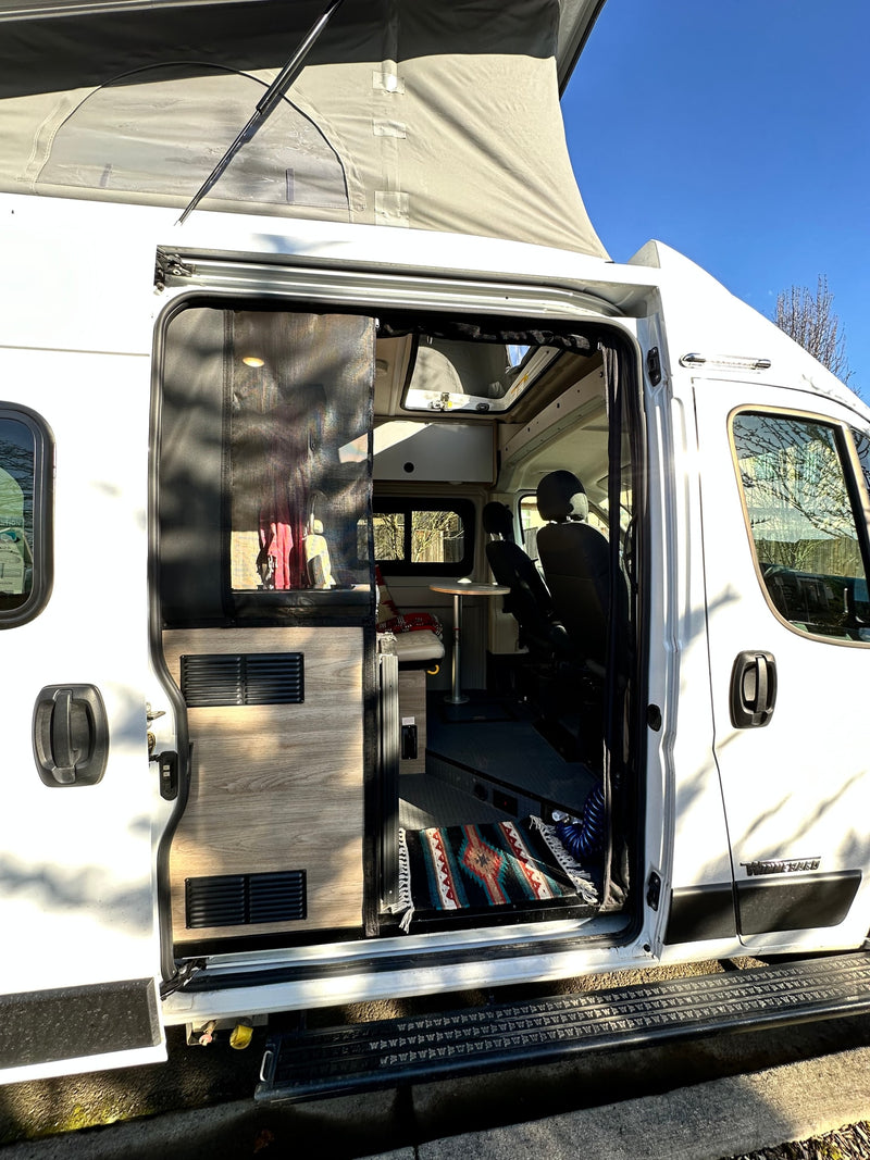 Open side door of an rv rental camper van reveals its pop-top roof and cozy interior with a table and rug. — photo 8