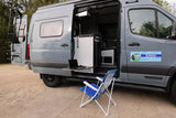 Grey Winnebago rv rental van, side open, featuring a pull-out laptop table and a blue camping chair for outdoor work.