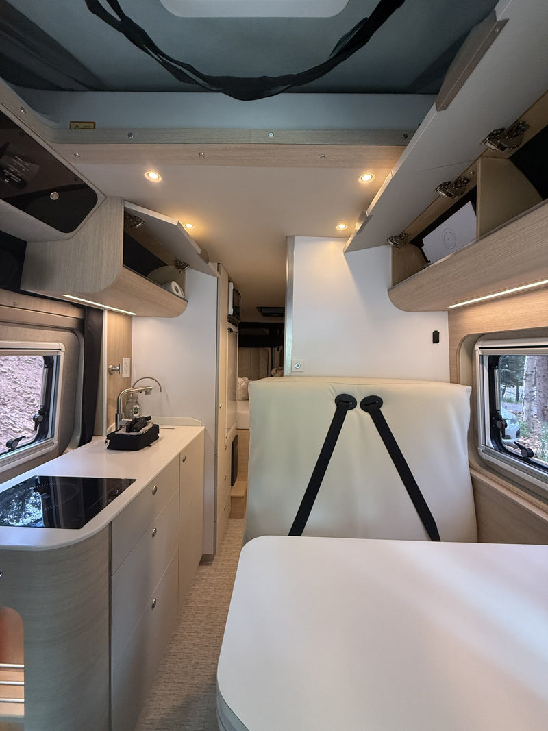Spacious rv rental interior showing kitchen, dining area, and bed setup with overhead storage and large windows. — photo 12