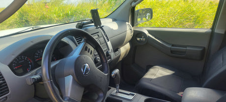 Inside a Nissan Xterra SUV: dashboard, steering wheel, passenger area. Parked in a sunny, grassy field. Perfect for outdoor trips or with an rv rental.