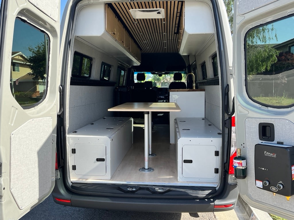 RV rental: Camper van interior reveals a versatile table, long storage benches, overhead cabinets, and rear water heater unit.