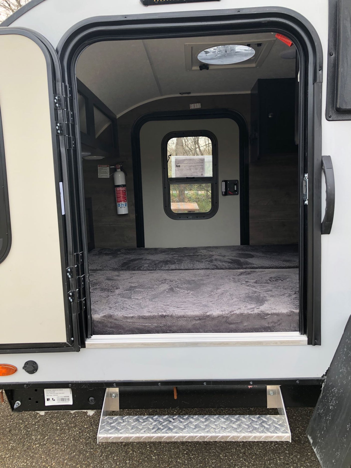 An open door shows the inviting interior of an RV rental, featuring a comfortable bed, fire extinguisher, and overhead vent.