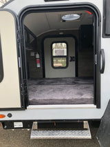 An open door shows the inviting interior of an RV rental, featuring a comfortable bed, fire extinguisher, and overhead vent.