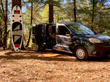 An Xterra SUP stands by a tree as a customized black Promaster City van offers cozy RV rental camping.