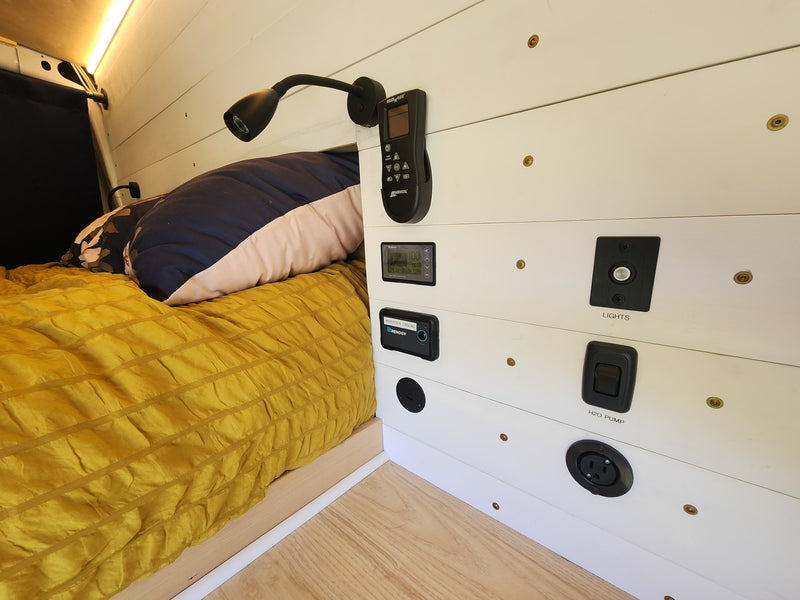 RV rental interior with a cozy bed, white shiplap walls, and a control panel featuring power monitor, inverter, and switches. — photo 8