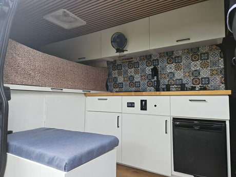 RV rental: Modern camper van interior featuring a colorful tiled kitchenette, Dometic fridge, and comfy blue cushion seating.