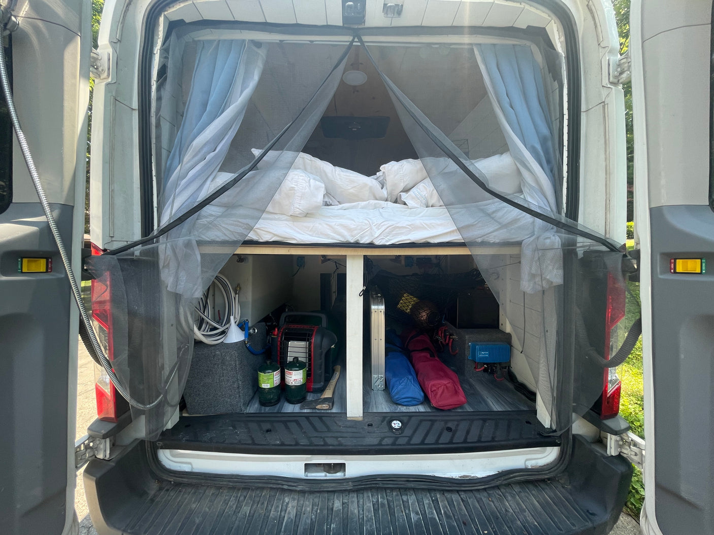 Experience van life with this RV rental! Rear interior of a camper van showing a cozy bed, under-bed storage, and a mosquito net.