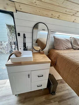Cozy RV rental interior with a compact vanity, sink, mirror, and comfortable bed, ideal for van life adventures.