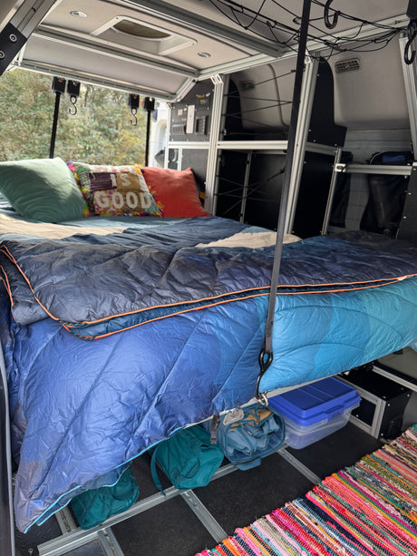 Cozy RV rental interior with a comfy bed, smart storage, and a colorful rug, perfect for mobile adventures.
