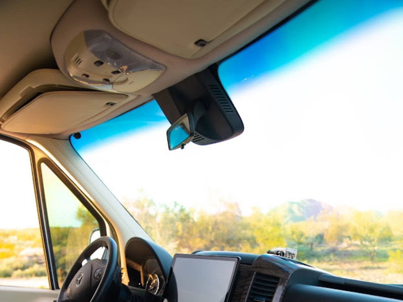 Inside an RV rental: driver's view of the dashboard, steering wheel, and sunny landscape through the windshield.