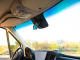 Inside an RV rental: driver's view of the dashboard, steering wheel, and sunny landscape through the windshield.