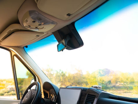Inside an RV rental: driver's view of the dashboard, steering wheel, and sunny landscape through the windshield.